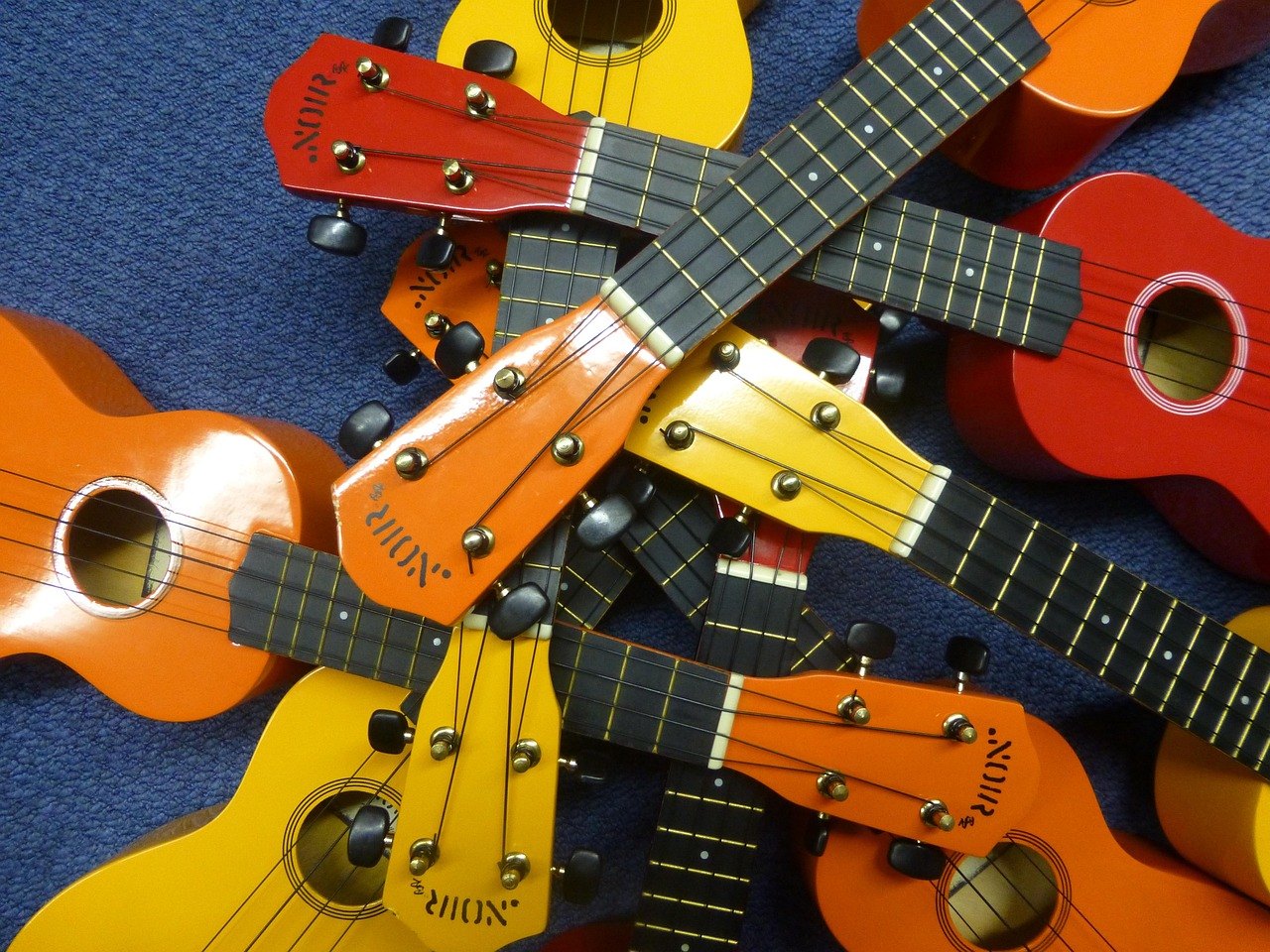 Ukulelen in Rot, Orange und Gelb, von oben auf blauem Stoff